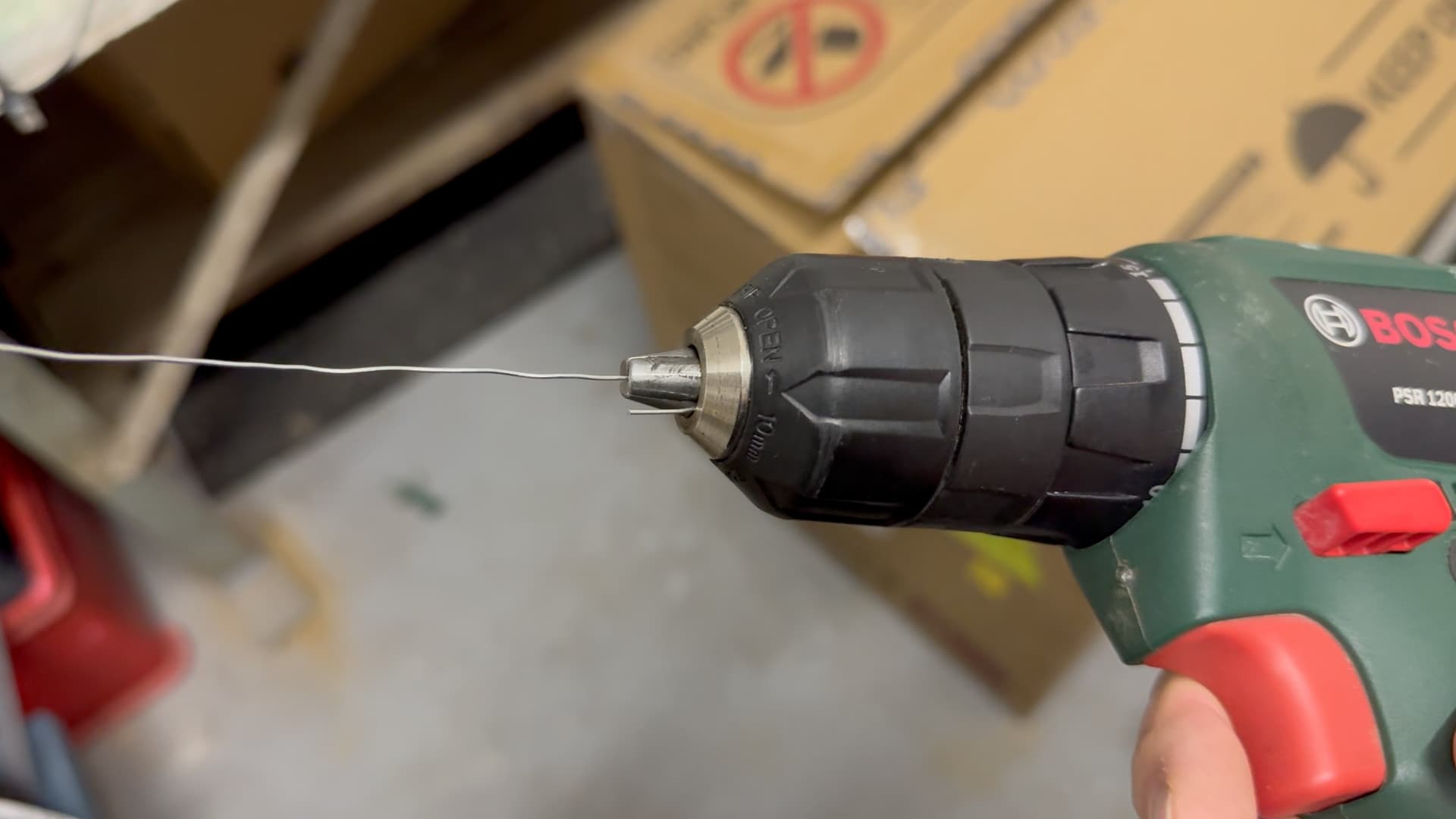 Ein Stück Basteldraht ist im Bohrfutter eines grünen Akkuschraubers eingespannt.